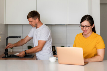 Husband and wife in the kitchen. Yuzh washes the dishes. Wife pays utility bills online