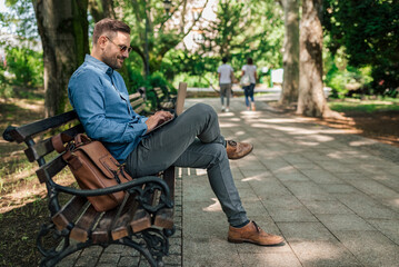 Fototapeta premium Joyful entrepreneur or businessman, sending an e-mail from the park bench.