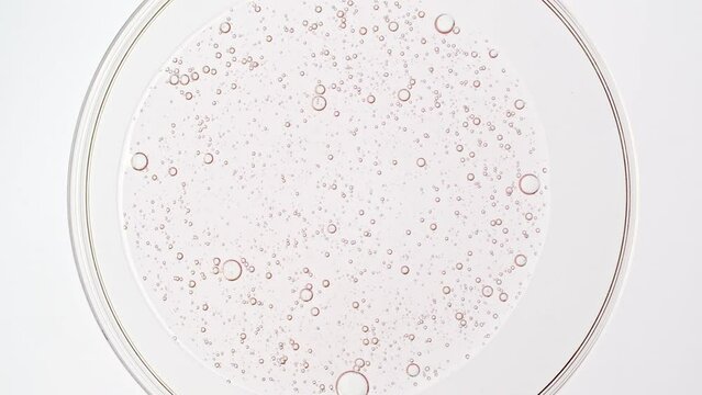 Transparent cosmetic pink gel fluid with molecule bubbles oil spreading out in petri dish. Macro Shot of Natural Organic Cosmetics, Medicine. Production Close-up. Slow Motion. High quality 4k footage