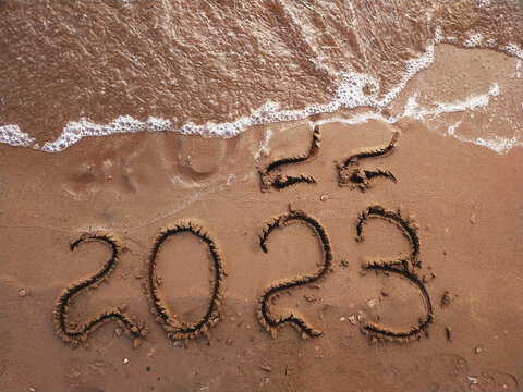Top view of the brown sandy shore of the reservoir, on which 2022 and 2023 were drawn with a stick, the outgoing 2022 was almost washed away by water in a wave with white foam, copy space.