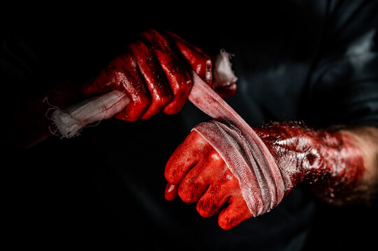 A man covered in blood bandages his hands.