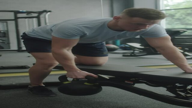 Vertical shot of muscular man in sportswear doing kettlebell single arm row exercise on bench while training in gym