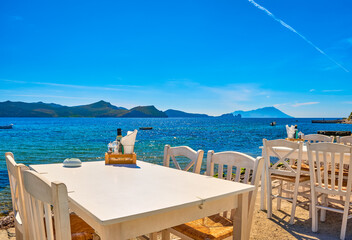 White chairs and tables of Greek tavern by waterfront at day