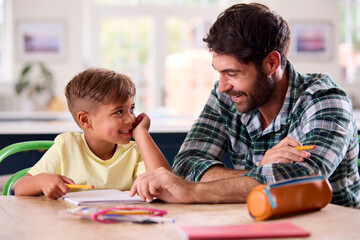 Father At Home In Kitchen Helping Son With Homework