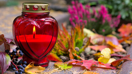 A red heart-shaped candle on a grave  in a cemetery on an autumn day. All Saints Day. Copy space,...