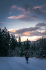 Girl hiking on a snowy trail during late sunset under the waning crescent moon on a cold winter day