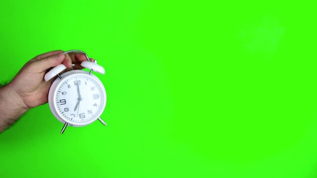 Green screen chroma key footage of a males hand holding and old fashioned alarm clock saying 7pm or 7am, filmed in 4k footage quality