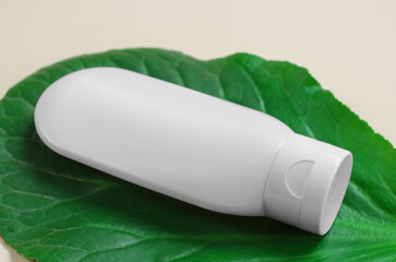 White plastic tube with hand, face, body cream on a large green leaf. Beauty skin care product template. White tube on a green leaf