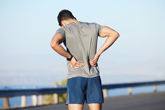 Fitness, tired and man with back pain in city while training cardio, marathon and health. Athlete runner with medical emergency for body while running, doing sports exercise and workout in the street