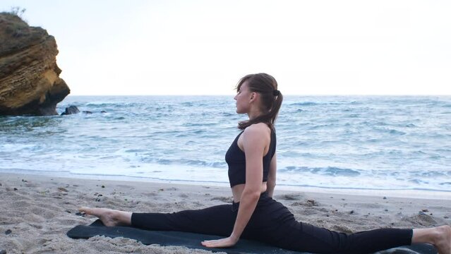 A caucasian young woman in a black sports suit doing yoga asana for woman's health care, on the ocean beach