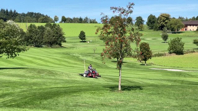 green keeper on lawn tractor mowing fairway on golf course