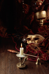 Burning candle in an old brass candlestick and carnival masks.