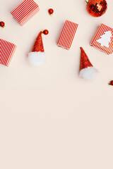 Fototapeta premium New Year holiday frame from Christmas decorations on beige background, red wrapped gift box, funny dwarfs, Christmas mirror ball, wooden fir tree, aesthetic festive concept, top view