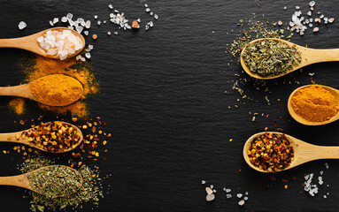 Obraz na płótnie Canvas Colored spices on wooden spoon on slate dark background with copy space