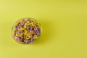 Cornflakes rings in a plate on a yellow background, top view.