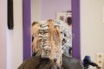 Woman in a hairdresser's waiting while coloring her hair. Faceless.