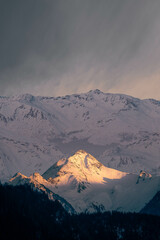 Peak of a mountain lit by the settling sun surrounded by a range of mountains