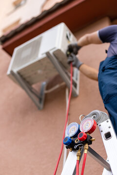 Worker maintains outdoor air conditioner using manometers for filling air conditioners.