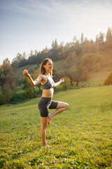 Woman stands barefoot on one leg and practices balancing with yoga breathing exercises.