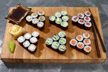 Assortment of different kinds of sushi rolls placed on black stone board. Sushi set with salmon, cucumbers, cream cheese, avocado and sesame seeds. Sushi image for menu