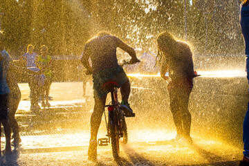  children splashing in the jets of the fountain in the summer heat at sunset