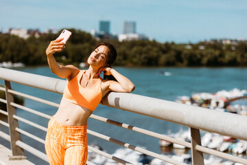 Happy beautiful woman in sportswear taking selfie with her smartphone on the bridge. Added grain film look effect
