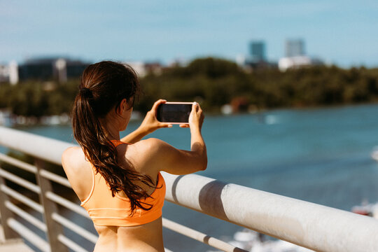 Back view portrait of a fitness woman taking photo of a landscape with mobile phone