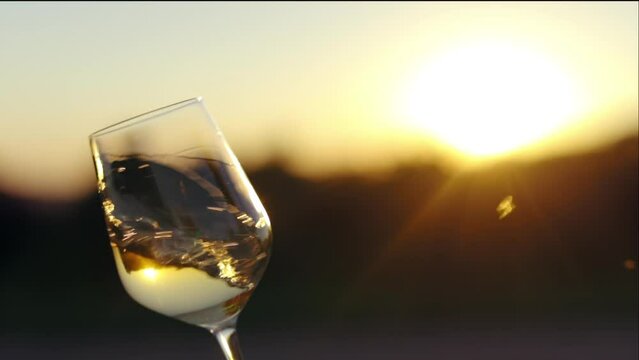 Sommelier swirls with a glass of white wine while tasting, outside at sunset