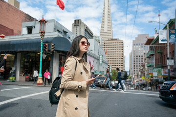 asian Taiwanese woman visitor holding phone using navigation app while crossing busy street in san Franciscoâs china town with chinese traditional lamp post at background