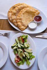 cheburek, deep fried turnover dish served with sauce, ketchup and fresh vegetable salad, traditional Crimean tatar cuisine, typical restaurant in Odesa, Ukraine, wooden table top view flat lay