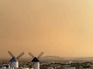 Pair of old windmills located in the town of Campo de Criptana (Spain), on the historic route of the mills of Don Quixote, during a dramatic misty sunset.