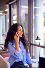 Fototapeta premium Businesswoman Standing By Partition In Open Plan Office Making Call On Mobile Phone