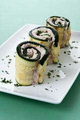 Grilled zucchini rolls stuffed with cream cheese and tuna on green background