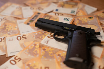 un pistolet est posé sur un gros tas de billets de banques qui recouvre l'ensemble de l'image