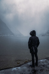Melancholic photo of a young man staring at the distant alpine village during a cold winter afternoon
