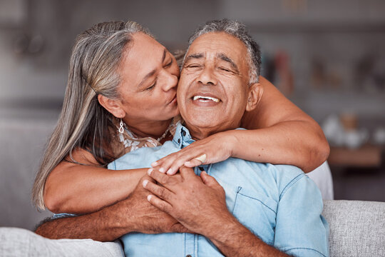 Happy senior couple hug in home, retirement lifestyle together in Mexico and relax on sofa. Romantic marriage life, love bonding time and elderly woman kissing latino husband on cheek in living room