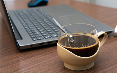 cup of coffee next to laptop on desk with selective focus