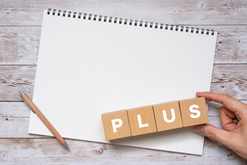 PLUSと書かれたブロック、ノート、ペン、手
