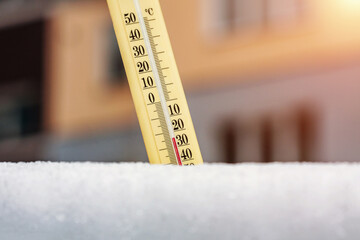 Wintertime. Thermometer in the snow shows very low temperatures against the background of a multi-storey building. Twenty four degrees under zero celsius. Concept of weather forecast.