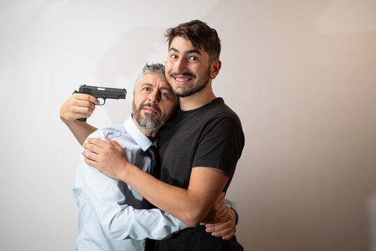 image drôle  d'un père dans les bras de son fils. Les deux sont souriant mais le fils pointe une arme sur la tempe de son père. Concept de complicité et d'amour