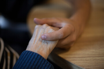gros plan sur la main d'un jeune homme tenant celle d'une personne âgée. Symbole de la compassion et de l'entraide intergénérationnelle