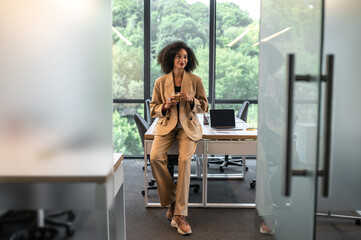 Good-looking businesswoman in beige suit with a cup of coffee in the office