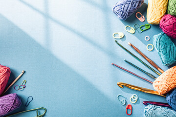 Crochet blue background with cotton yarn, crochet hooks and accessories. Flat lay overhead shot with copy space. Window shadow, toned photo
