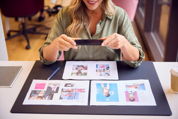 Close Up Of Businesswoman Sitting At Desk Taking Photo Of Proofs Or Design Layouts On Mobile Phone