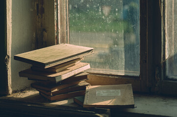 Somewhere in an abandoned house, old dusty books and ledgers are lying on a dirty windowsill, the light of the evening sun is coming through the dirty window