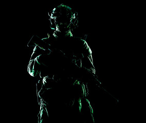 Army special forces elite soldier with hidden behind mask and glasses face, battle helmet, tactical radio headset, standing with assault rifle equipped silencer in darkness, contour shot