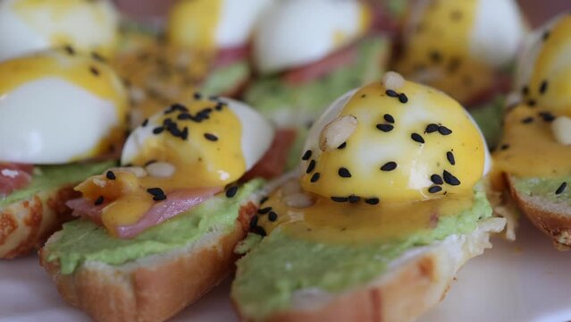 Delitious toast with salmon, boiled egg and guacamone on a white plat sprinkled pine nuts and black cumin. Close-up slow motion video