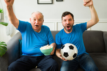 Cheerful senior man and caucasian man celebrating their soccer team win