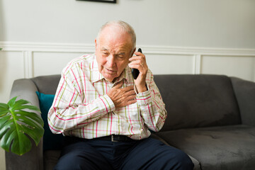 Sick elderly man calling emergency on the phone because of a heart attack