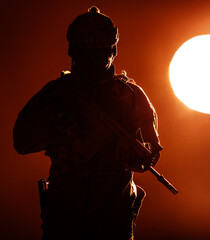 Army soldier in Protective Combat Uniform holding Special Operations Forces Combat Assault Rifle operating at sunset lit by evening sun